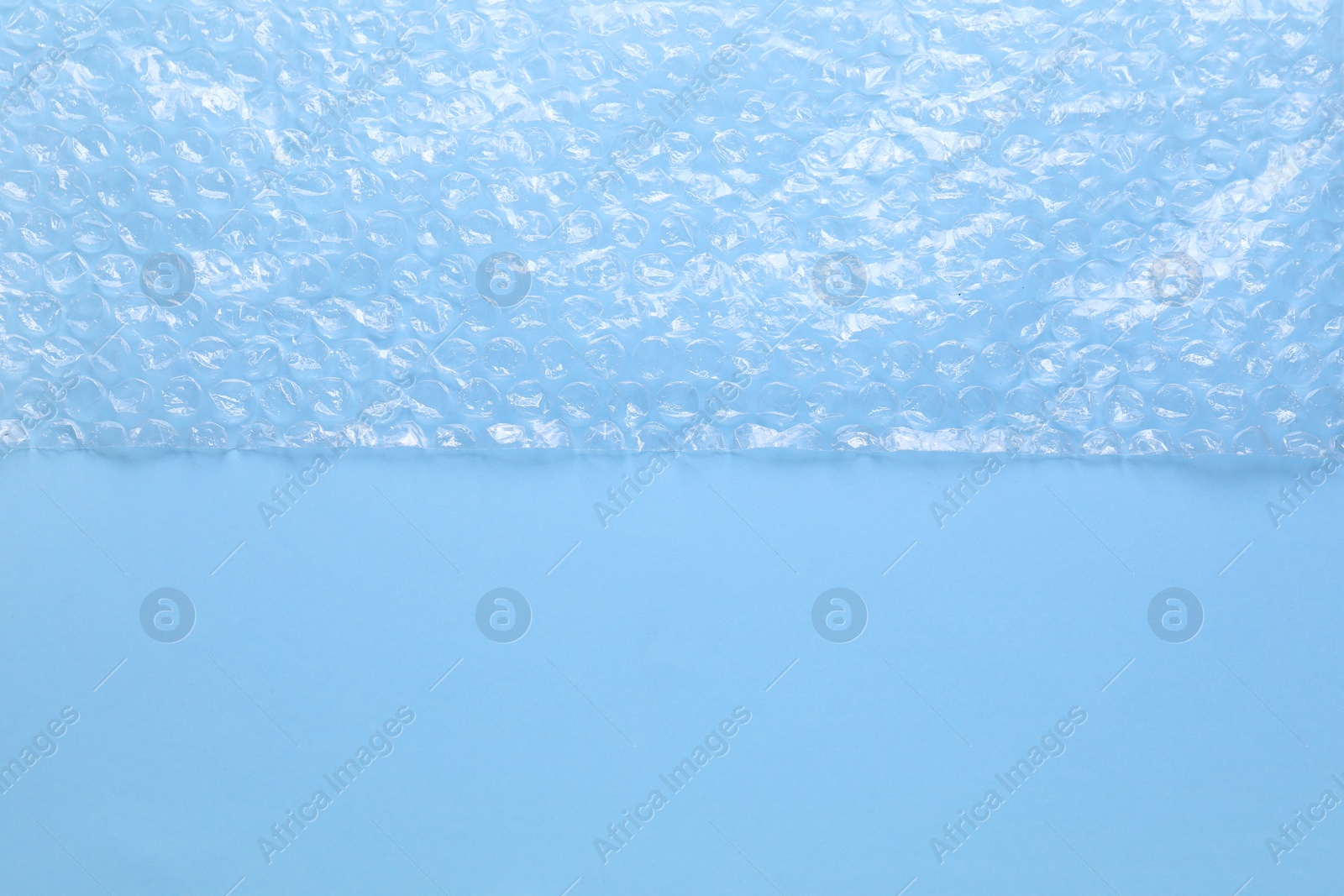 Photo of Transparent bubble wrap on light blue background, top view. Space for text