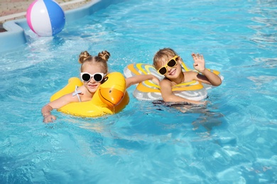Photo of Happy children with inflatable rings in outdoor swimming pool on sunny summer day