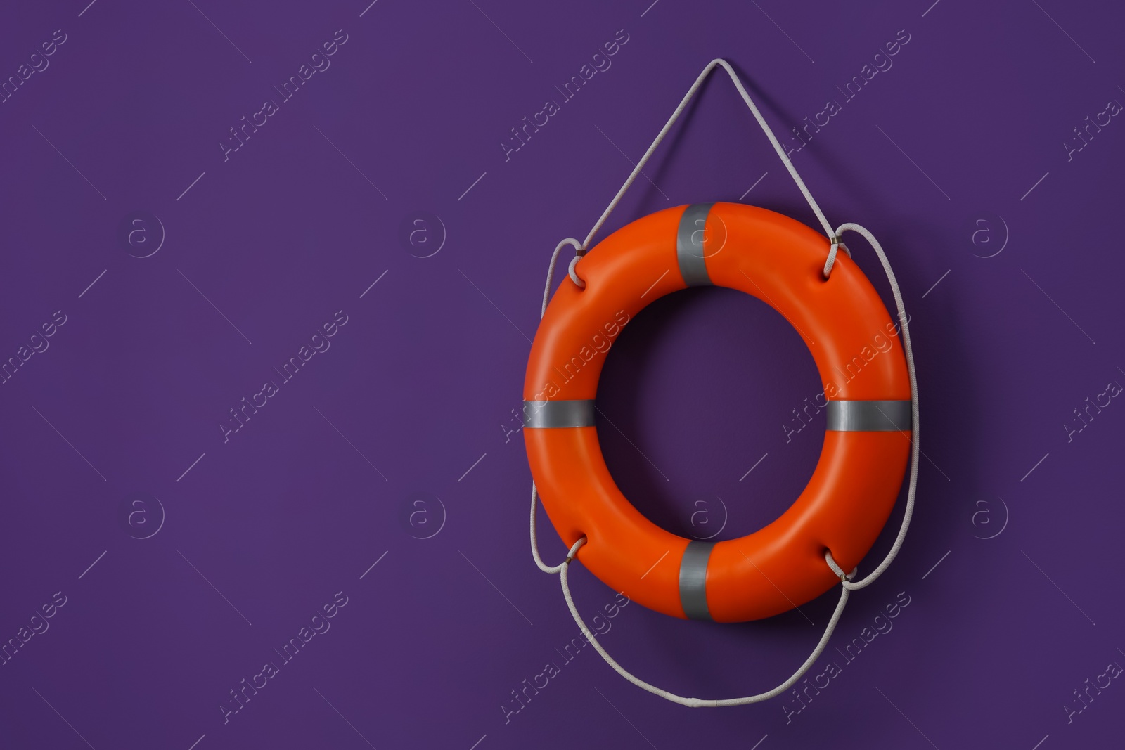 Photo of Orange lifebuoy and space for text on violet background. Rescue equipment