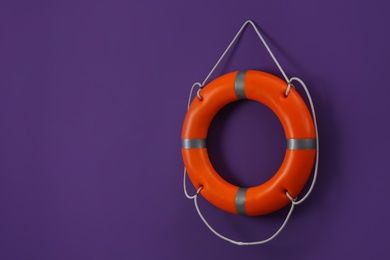 Orange lifebuoy and space for text on violet background. Rescue equipment