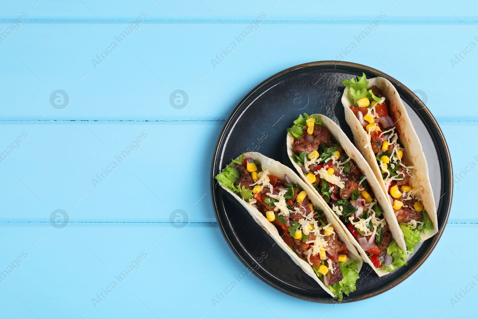 Photo of Delicious tacos with meat and vegetables on light blue table, top view. Space for text