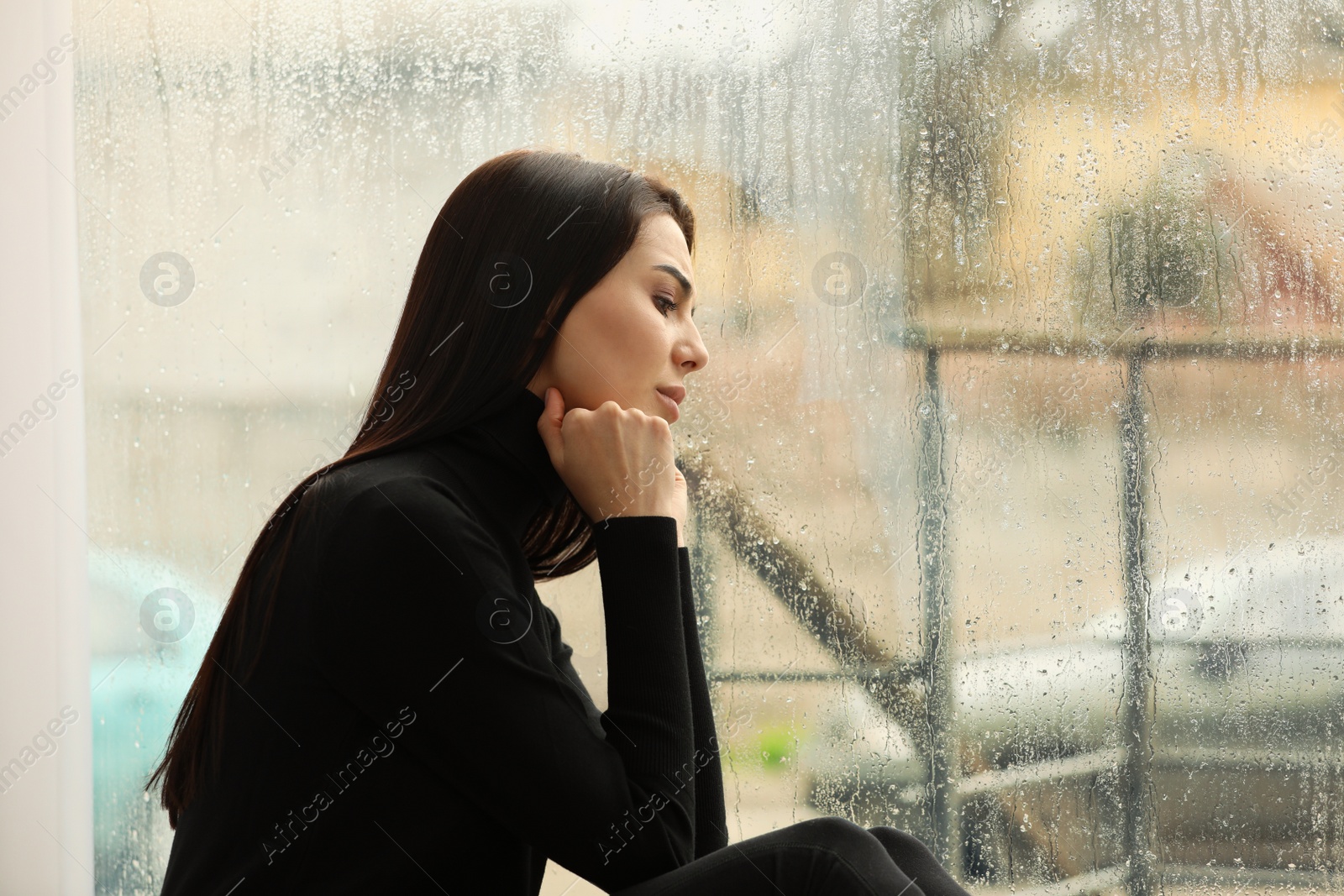 Photo of Depressed woman near window on rainy day, space for text