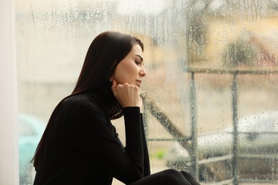 Photo of Depressed woman near window on rainy day, space for text