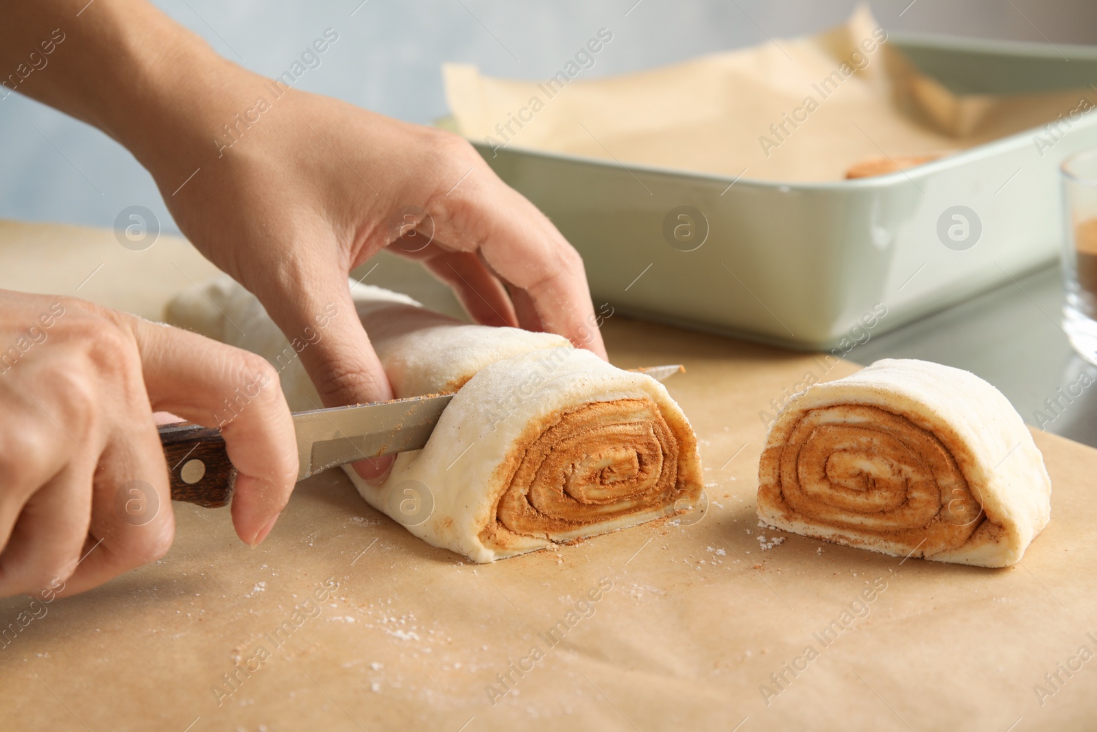 Photo of Woman cutting dough for cinnamon rolls on parchment at table, closeup
