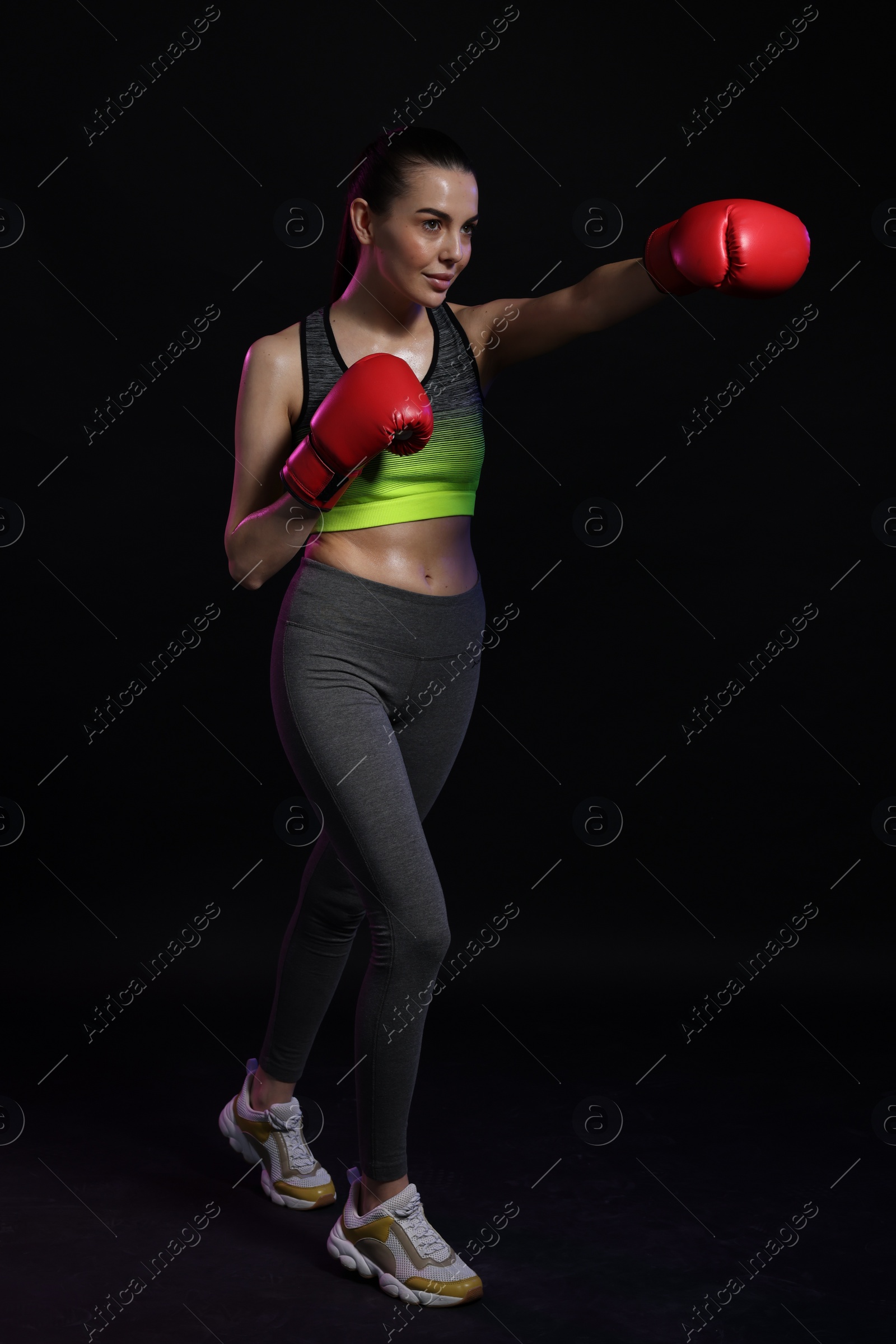 Photo of Beautiful woman in boxing gloves training on black background