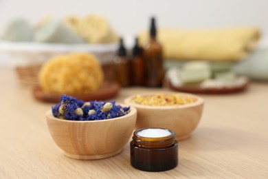 Photo of Bowls with dry flowers and jar of cream on light wooden table. Spa therapy