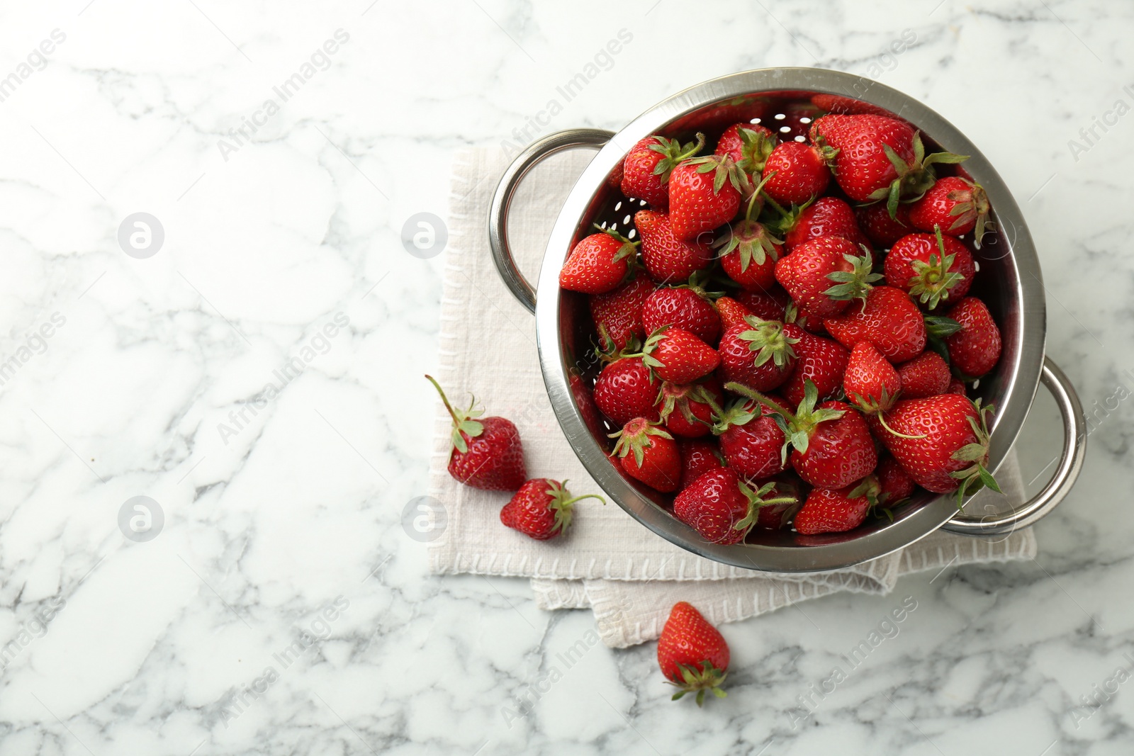 Photo of Metal colander with fresh strawberries on white marble table, top view. Space for text