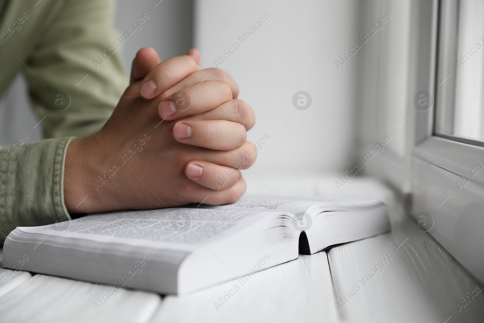 Photo of Religion. Christian man praying over Bible at white wooden the table, closeup