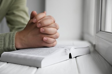 Photo of Religion. Christian man praying over Bible at white wooden the table, closeup