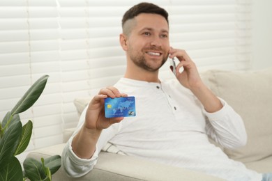 Happy man with credit card using smartphone for online shopping on sofa at home, selective focus