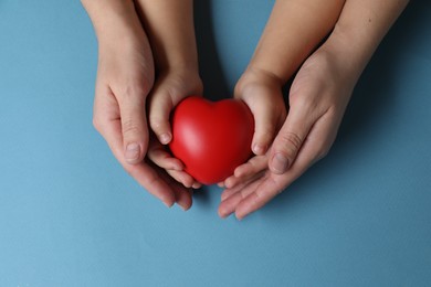 Photo of Mother and her child holding red decorative heart on light blue background, top view