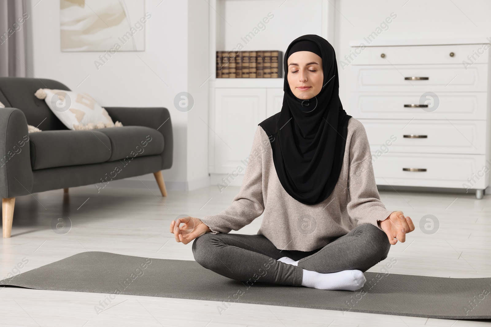 Photo of Muslim woman in hijab meditating on fitness mat at home. Space for text