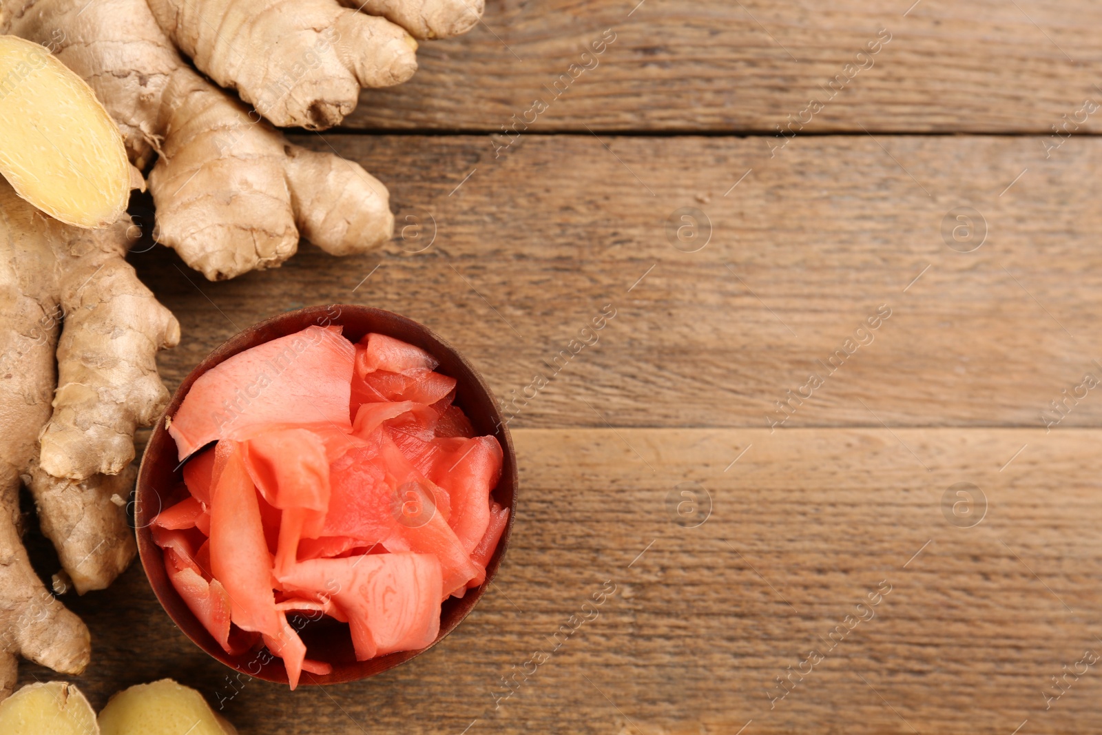 Photo of Spicy pickled ginger and root on wooden table, flat lay. Space for text