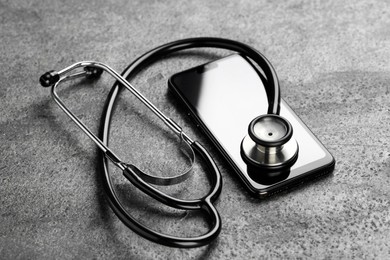 Modern smartphone and stethoscope on grey table