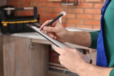 Photo of Male plumber writing in clipboard indoors, closeup. Repair service