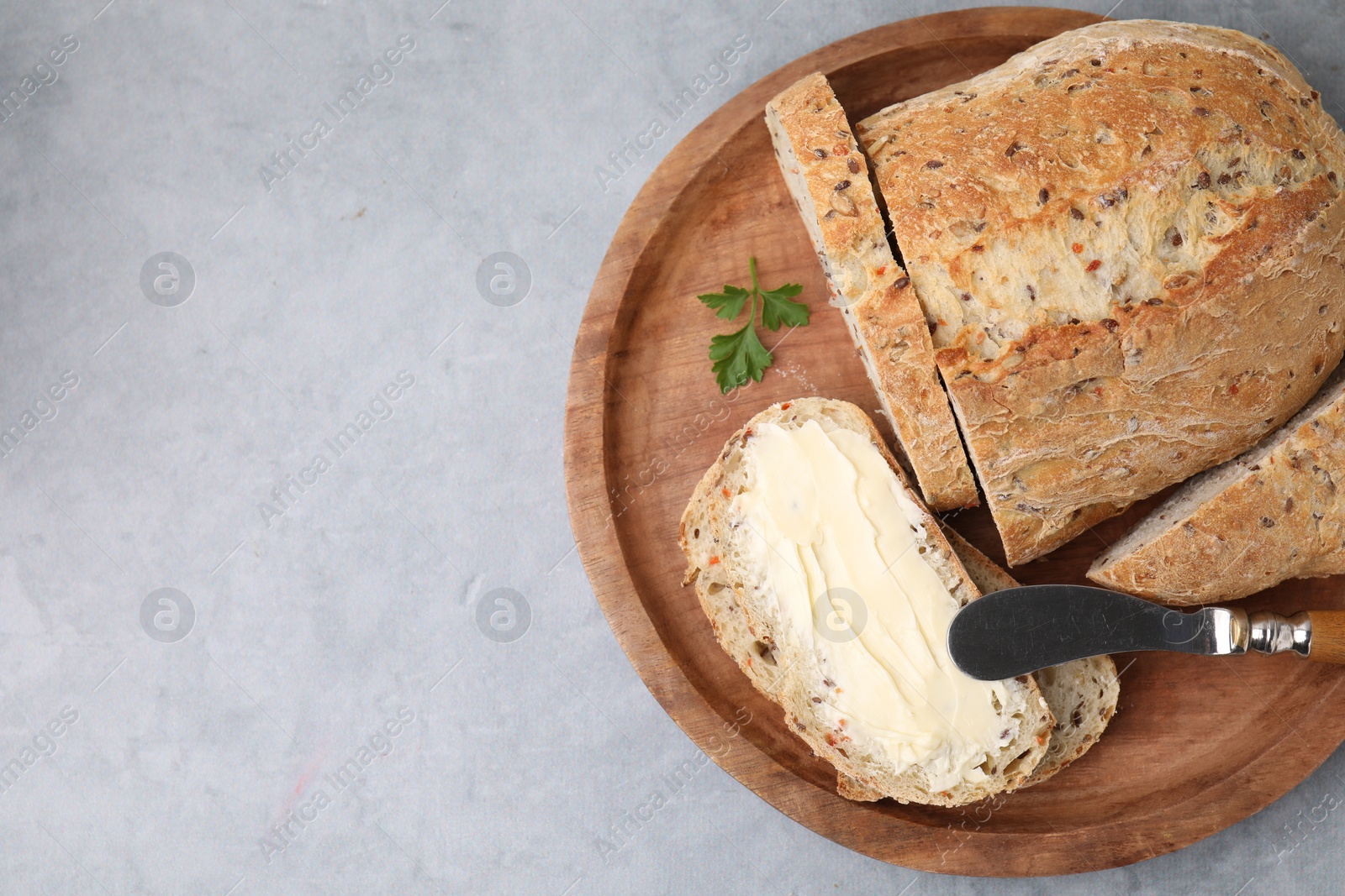 Photo of Tasty bread with butter and knife on grey textured table, top view. Space for text