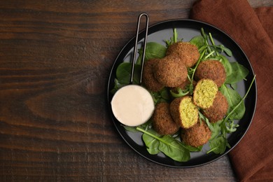 Photo of Delicious falafel balls, herbs and sauce on wooden table, top view. Space for text