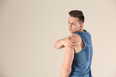 Man in sportswear suffering from shoulder pain on light background