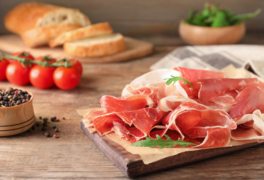 Photo of Pile of tasty prosciutto on wooden table