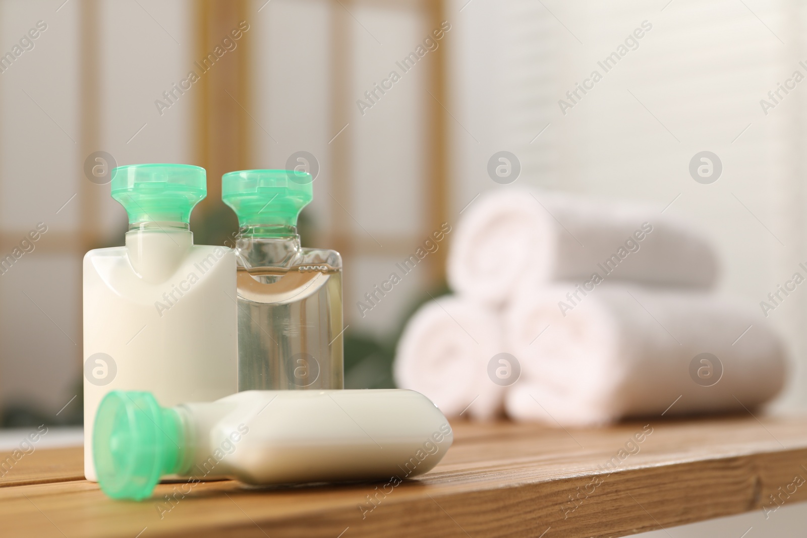 Photo of Wooden tray with mini bottles of cosmetic products on bath tub in bathroom. Space for text