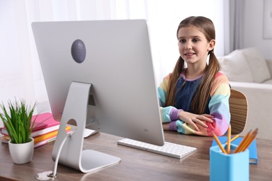Photo of E-learning. Cute girl using computer during online lesson at table indoors