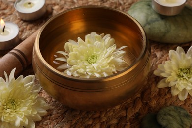 Photo of Tibetan singing bowl with water, beautiful chrysanthemum flowers, mallet and burning candle on table, closeup