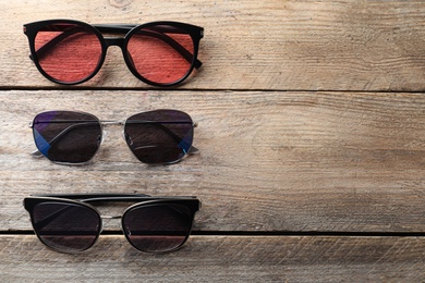 Many stylish sunglasses on wooden background, flat lay. Space for text