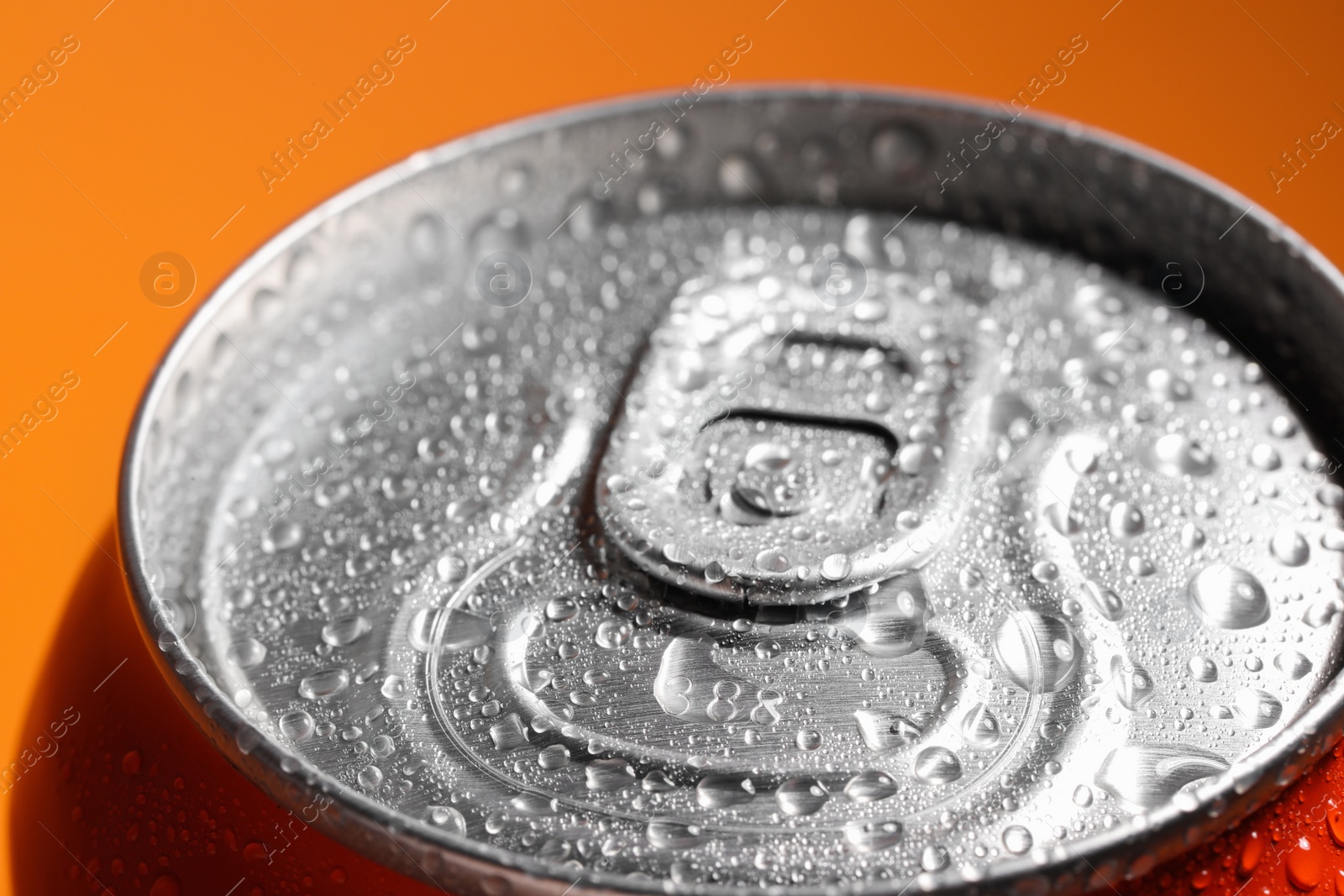 Photo of Aluminum can of beverage covered with water drops on orange background, closeup