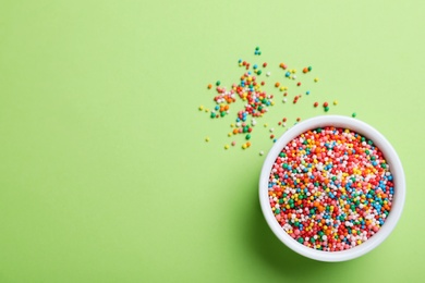 Photo of Colorful sprinkles and bowl on green background, flat lay with space for text. Confectionery decor