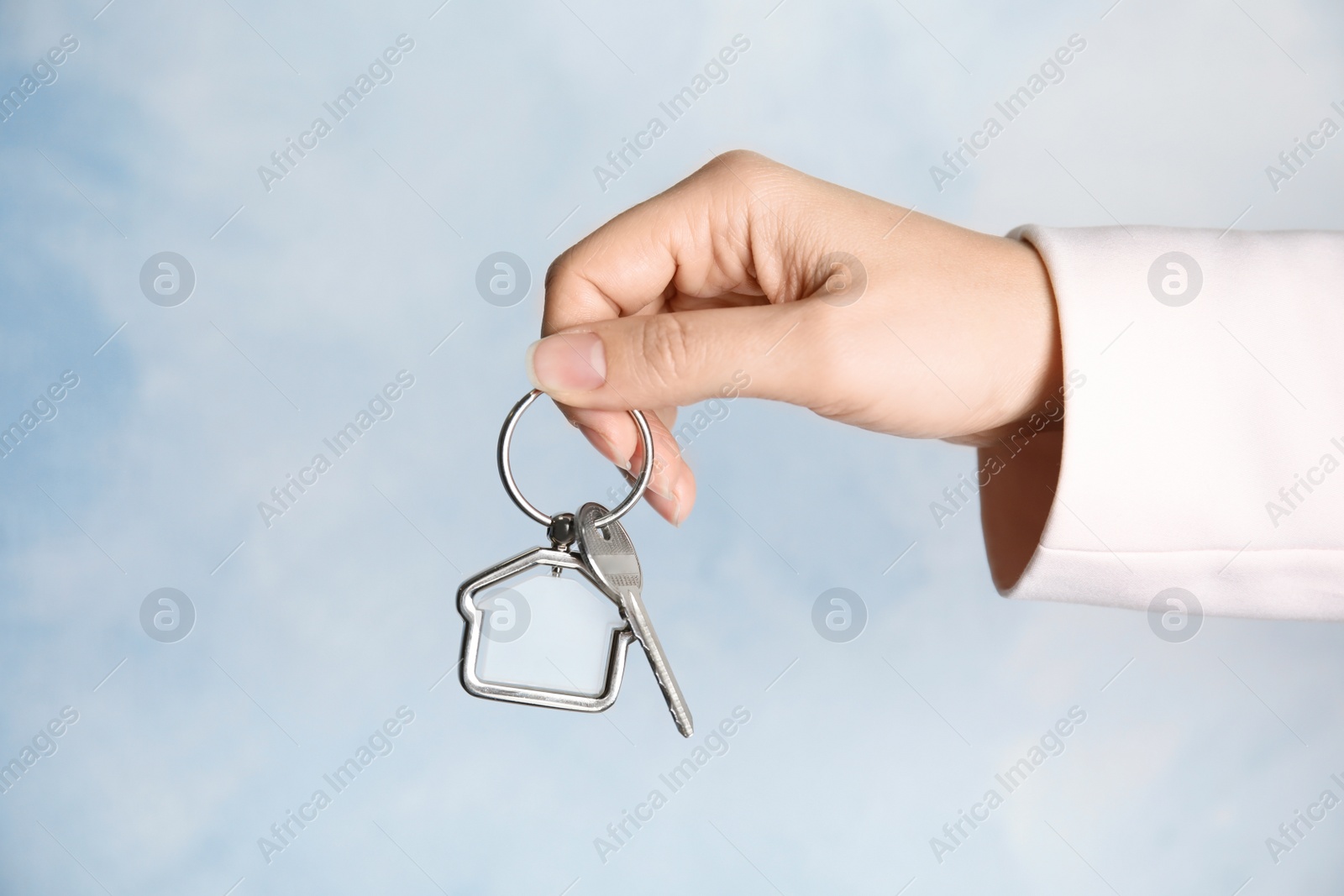 Photo of Woman holding house key with trinket on color background, closeup