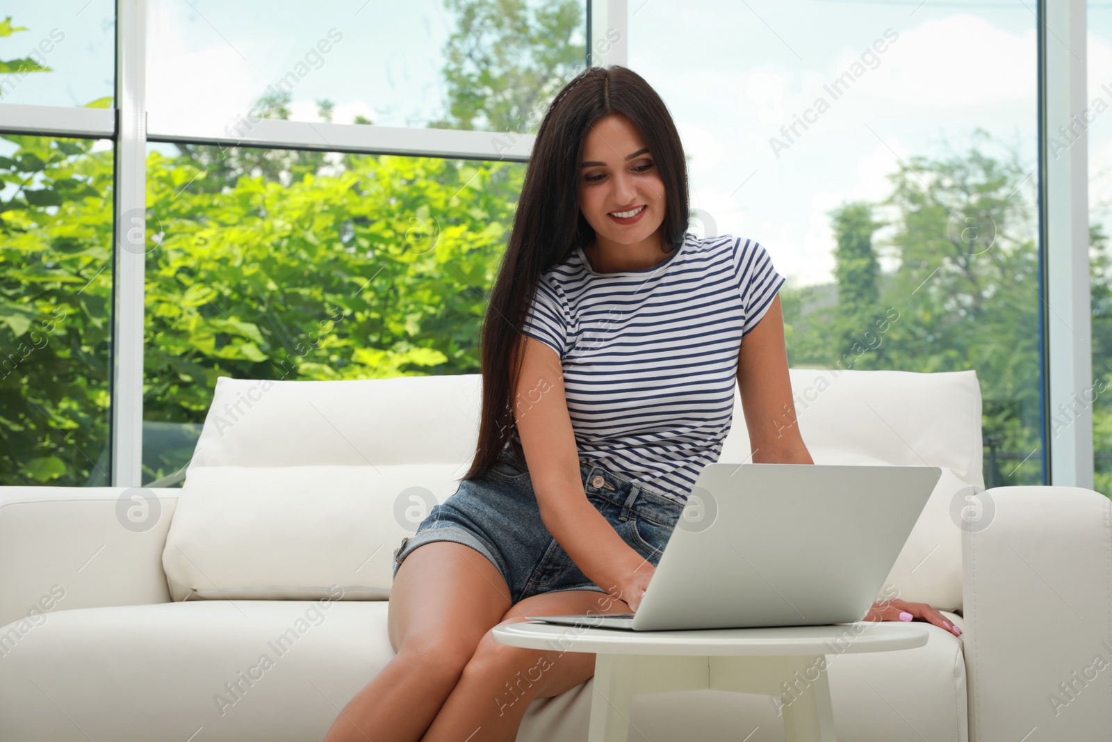 Photo of Young woman using laptop on sofa at home. Internet shopping