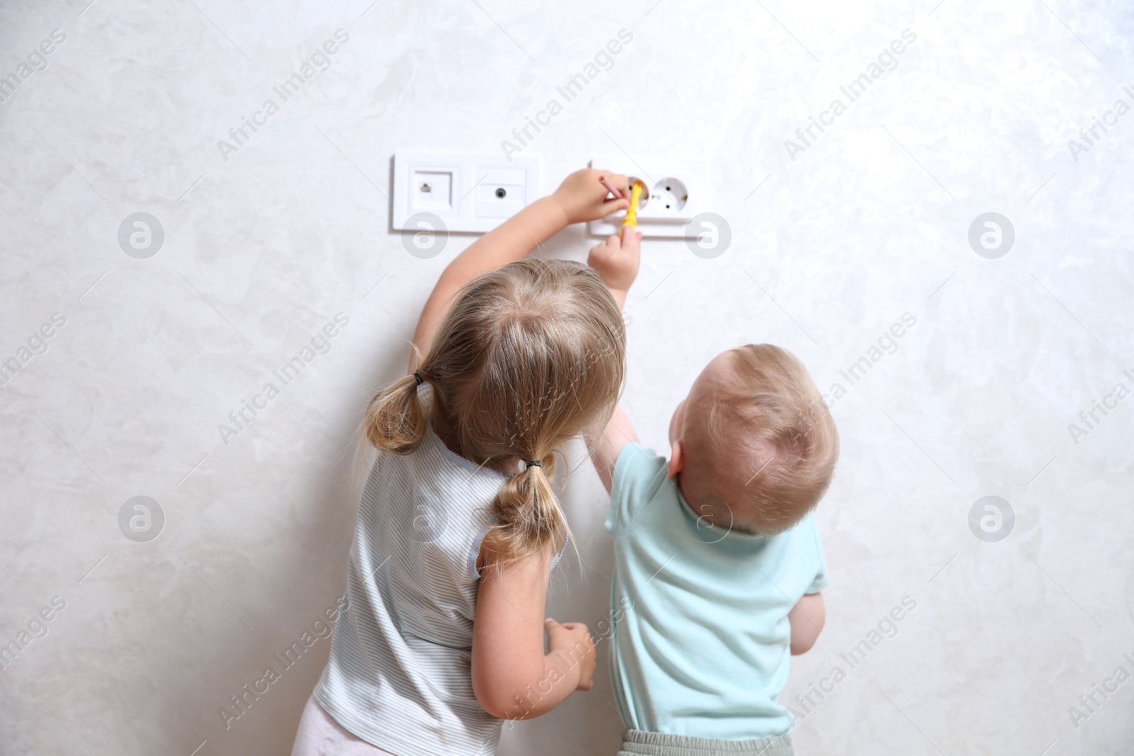 Photo of Little children playing with electrical socket indoors, back view. Dangerous situation