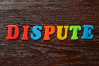 Photo of Word Dispute made of colorful letters on dark wooden table, flat lay