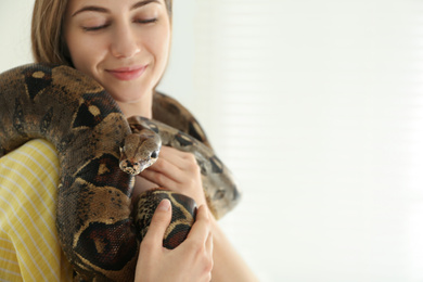 Young woman holding boa constrictor on light background, closeup. Exotic pet