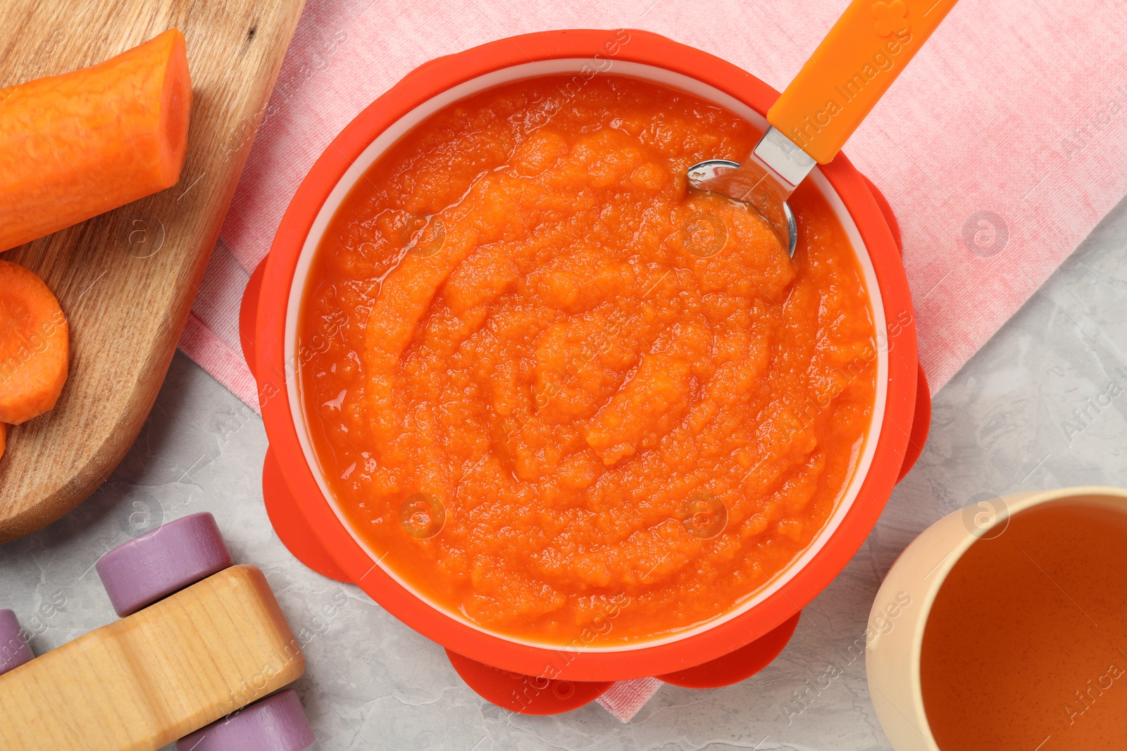 Photo of Healthy baby food. Bowl with delicious carrot puree on light grey marble table, flat lay