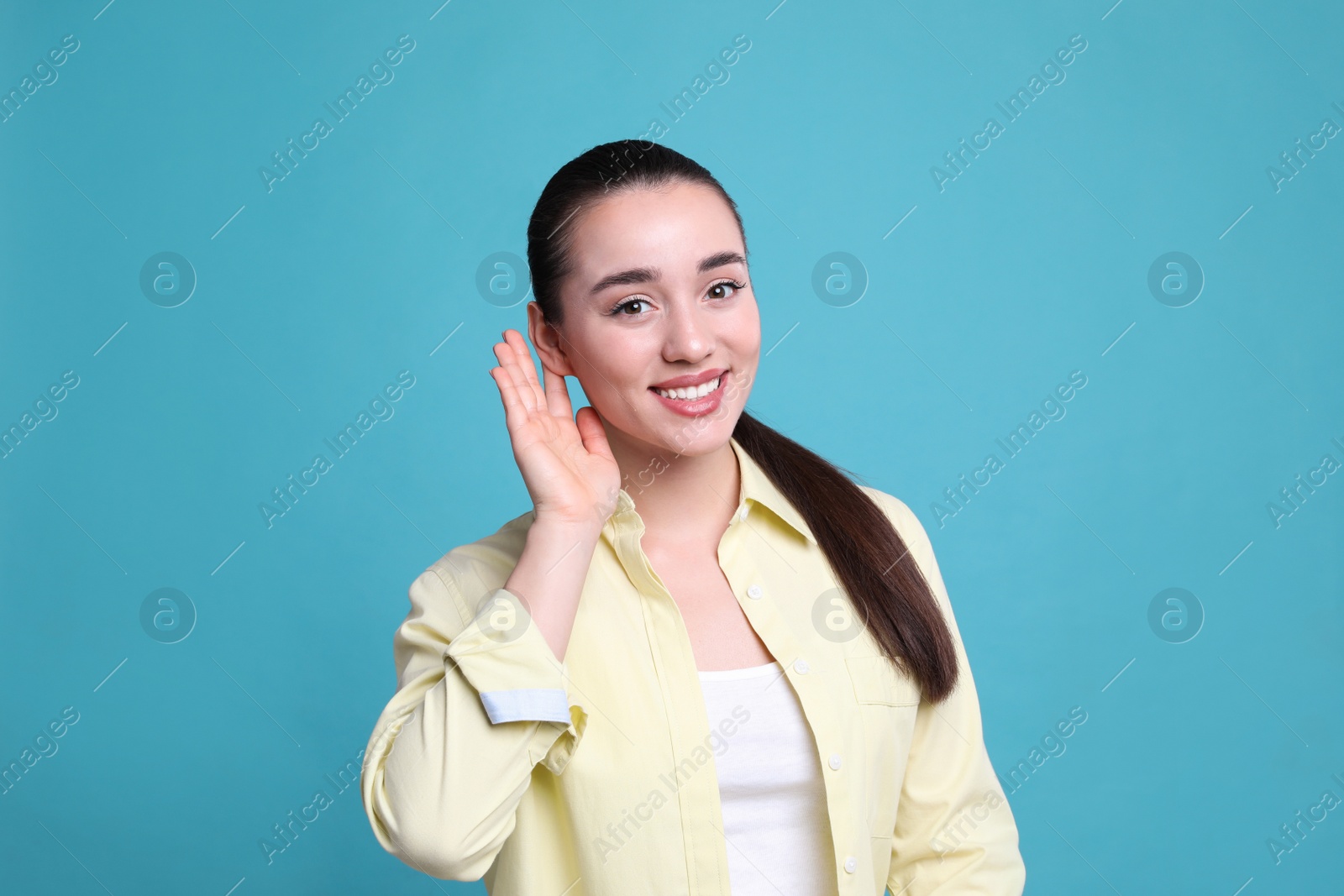 Photo of Young woman showing hand to ear gesture on light blue background