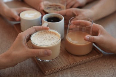 Photo of Friends drinking coffee at wooden table in cafe, closeup