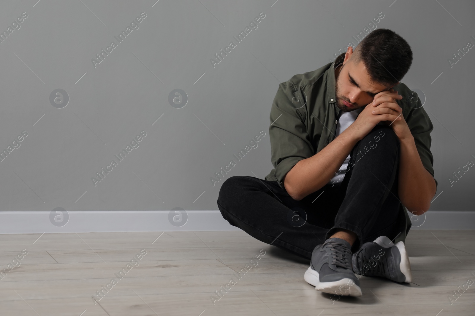 Photo of Sad man sitting on floor near light grey wall. Space for text