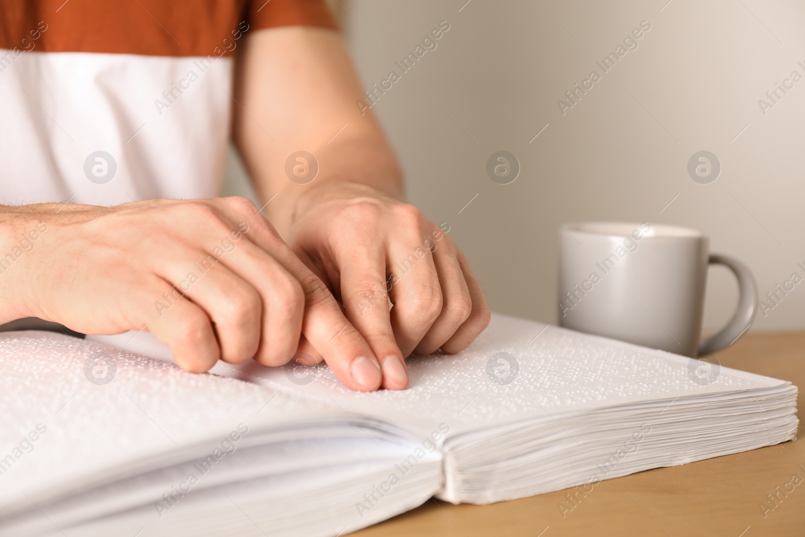 Photo of Blind man reading book written in Braille at table, closeup