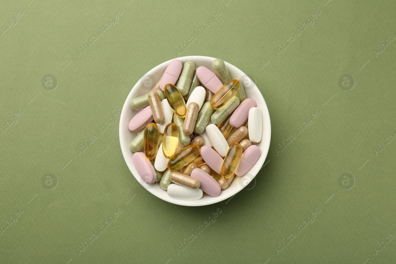 Photo of Different vitamin pills in bowl on olive background, top view