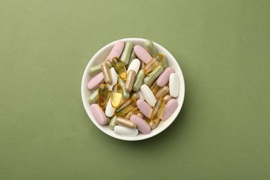 Different vitamin pills in bowl on olive background, top view