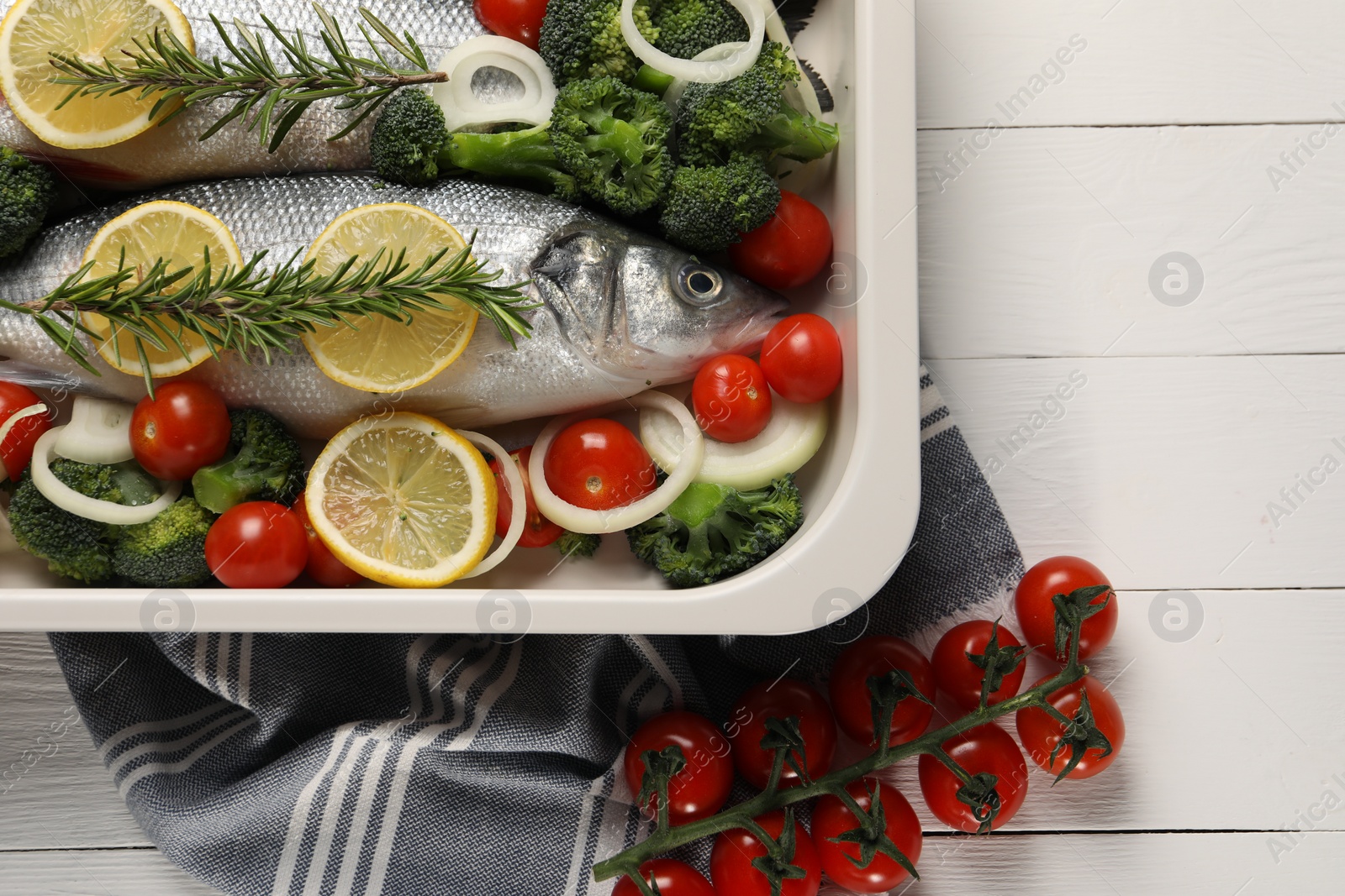 Photo of Raw fish with lemon in baking dish and vegetables on white wooden table, flat lay. Space for text