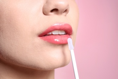 Photo of Beautiful young woman applying gloss on her perfect lips, closeup