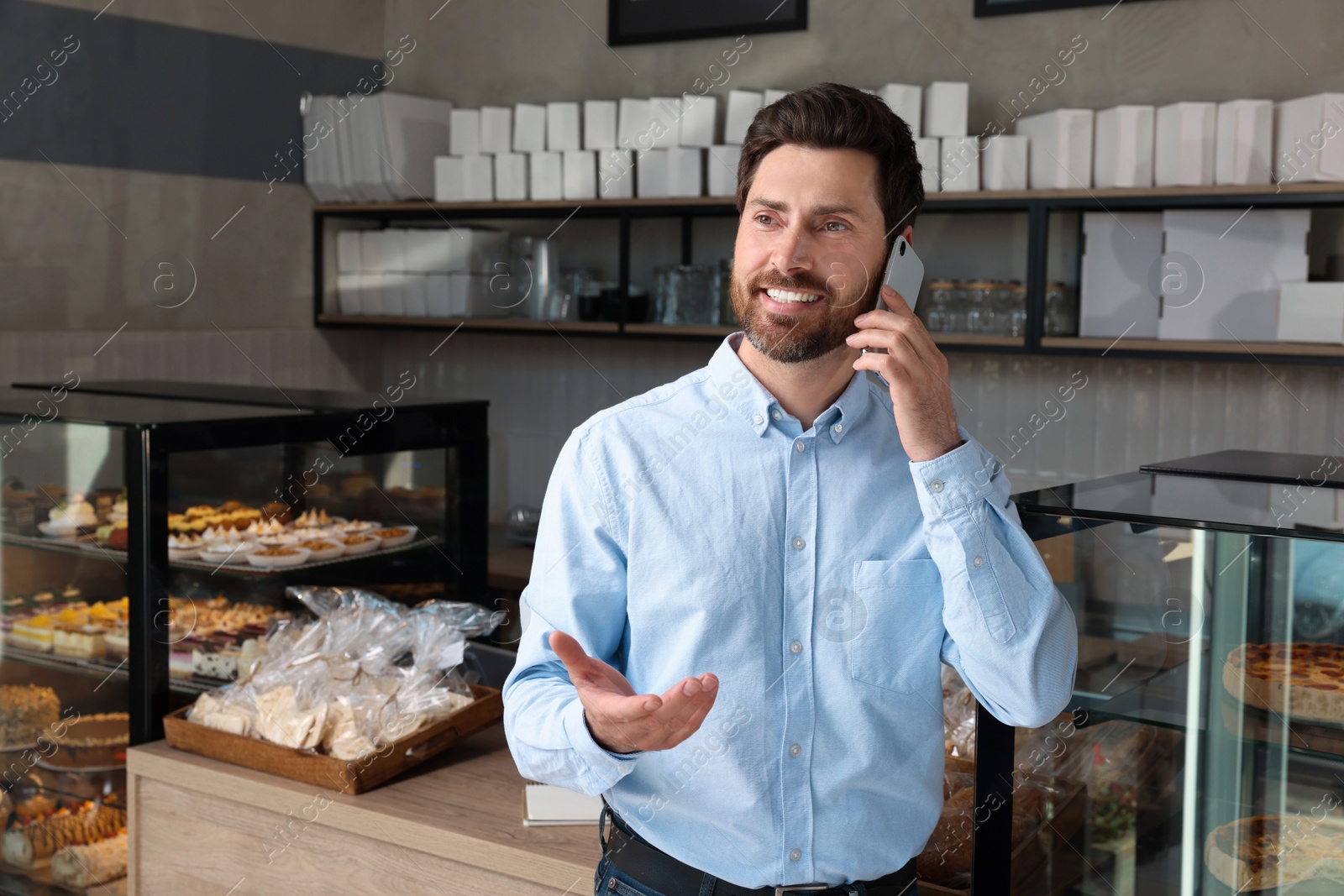 Photo of Happy business owner talking on phone in bakery shop