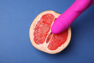 Photo of Half of grapefruit and purple vibrator on blue background, flat lay. Sex concept