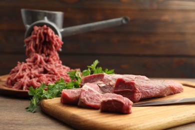 Manual meat grinder with beef and parsley on wooden table