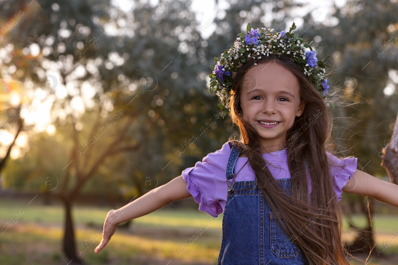 Photo of Cute little girl wearing flower wreath outdoors. Child spending time in nature