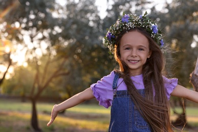 Cute little girl wearing flower wreath outdoors. Child spending time in nature