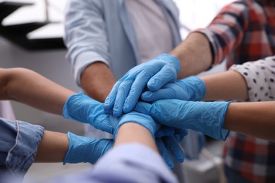 Photo of Group of people in blue medical gloves stacking hands indoors, closeup