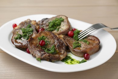 Tasty beef tongue pieces, salsa verde and berries on beige wooden table, closeup